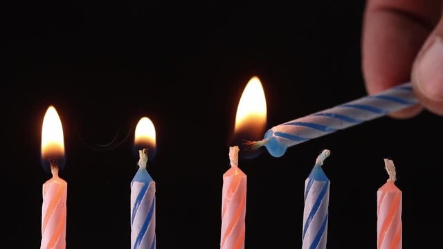 hand lighting up five birthday candles on black background