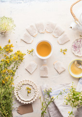 Cup with frame of tea bags of herbal tea on white table background, top view. Herbal tea setting with teapot , honey and fresh medical herbs and flowers. Copy space. Healthy preventive drink treatment
