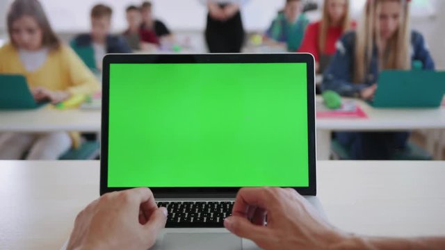 Close-up of man using a mock up green screen laptop teaching students in the classroom. View of focused young students working by computers in a science class at school.