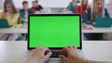 Close-up of male hands of a teacher typing on laptop keyboard with mockup screen sitting in the classroom. View of clever students working on computers during a lesson in a modern school. - Powered by Adobe