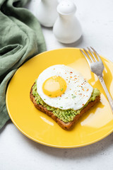 Toast with fried egg and avocado on yellow plate. Tasty breakfast, lunch or snack
