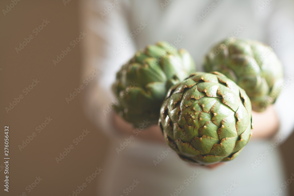 Wall mural the girl holds in her hands an artichoke with a blur of the background, the concept of proper and di