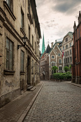 The narrow cobbled street of old Riga in  Latvia with not renovated dilapidated and shabby houses overlooking the spire of the Cathedral of St. James