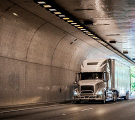 Big rig gray semi truck transporting cargo in dry van semi trailer running in arched tunnel laid...