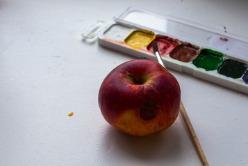 a red apple and watercolor paint and brush on white background