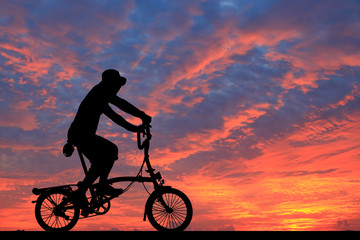 Obraz premium Silhouette man and bike relaxing on blurry sunrise sky background.