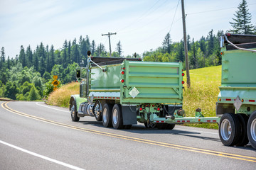 Big rig tip truck with two dump trailer driving on the road with hills and trees