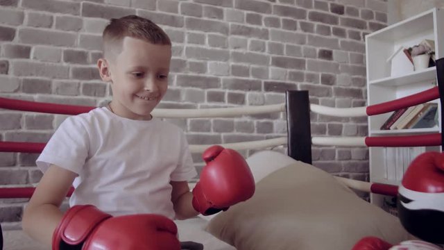 The father is training his son boxing. In the hands of the boy redboxing gloves. They go in for sports at home.
