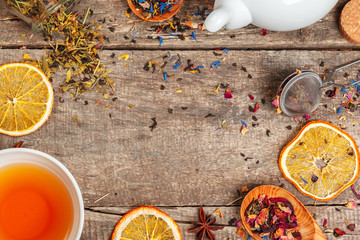 cups of healthy herbal tea with cinnamon, dried rose and camomile flowers in spoons over wooden background, top view