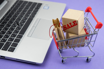 Shopping cart with purchases for sale - packages and boxes on the modern laptop. Online shopping...