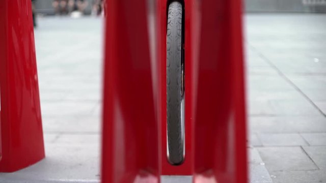 Red bicycle docks in the centre of Barcelona. Wheels and metallic parts of a bike stations. People walking around the square near museum of contemporary art. 
