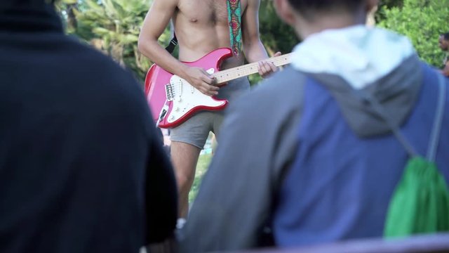 Man playing guitar in a city park. Urban activities in Barcelona central parc Ciutadella. Red guitar. No shoes on. 