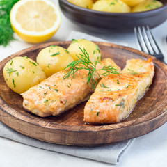 Baked salmon in creamy sauce with young boiled  potato topped with melted butter and chopped dill on  wooden plate, square format