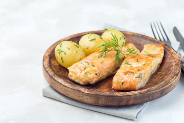 Baked salmon in creamy sauce with young boiled  potato topped with melted butter and chopped dill on  wooden plate, horizontal, copy space