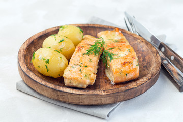 Baked salmon in creamy sauce with young boiled  potato topped with melted butter and chopped dill on a wooden plate, horizontal