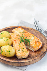 Baked salmon in creamy sauce with young boiled  potato topped with melted butter and chopped dill on wooden plate, vertical, copy space