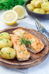 Baked salmon in creamy sauce with young boiled  potato topped with melted butter and chopped dill on wooden plate, vertical