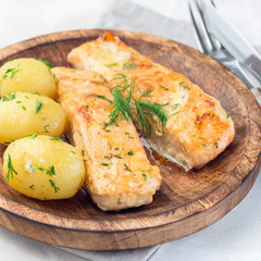Baked salmon in creamy sauce with young boiled  potato topped with melted butter and chopped dill on  wooden plate, square format