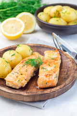 Baked salmon in creamy sauce with young boiled  potato topped with melted butter and chopped dill on  wooden plate, vertical
