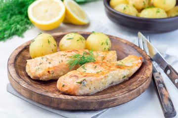 Baked salmon in creamy sauce with young boiled  potato topped with melted butter and chopped dill on wooden plate, horizontal