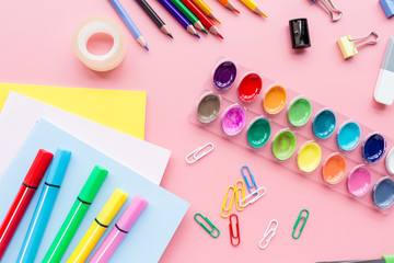 School supplies stationery, colour pencils, paints, paper on pink background, back to school concept with free copy space for text, modern elementary education. Kids desk, flat lay, top view, mockup.