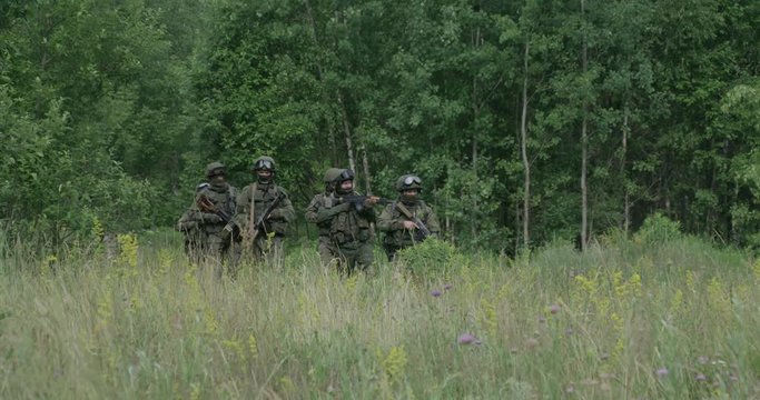 Soldiers in camouflage with assault rifle walking through the field military action in the steppe area, 4k slow motion.