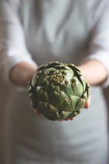 The girl is holding an artichoke with a blurred background, the concept of proper and dietary...