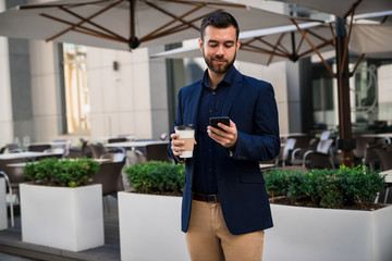 Confident young Businessman texting and drinking coffee in front of caffee outddoor.