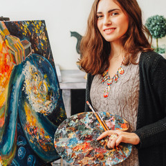 Talented female painter holding palette, performing colorful abstract artwork in studio.