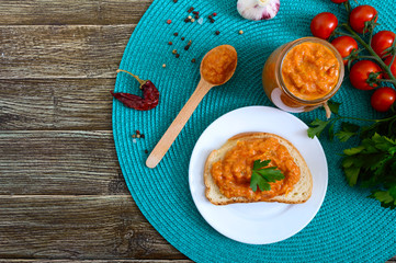 Delicious squash caviar in a jar and spread on slices of white bread on the table. Homemade caviar with zucchini, garlic, carrots, tomato sauce. Vegan cuisine. The top view. Flat lay