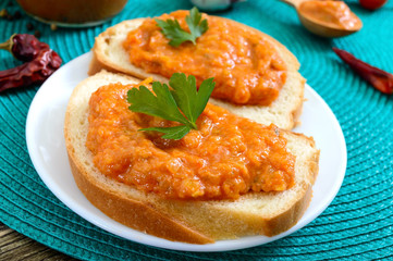 Delicious squash caviar in a jar and spread on slices of white bread on the table. Homemade caviar with zucchini, garlic, carrots, tomato sauce. Vegan cuisine. Close up