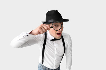 Male detective with magnifying glass on light background