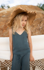 Little cute girl in stylish clothes on a background of rocks. Summer portrait of a little girl in a hat and cotton clothes for a magazine or advertisement