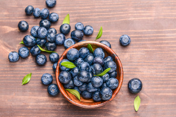 Bowl with ripe blueberry on wooden background