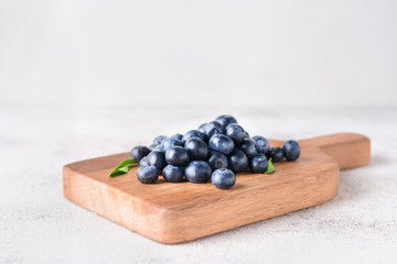 Board with ripe blueberry on light background