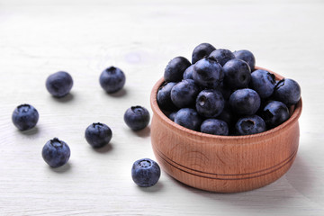 Tasty ripe blueberry berries in a wooden bowl on a white wooden table.
