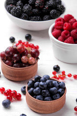Delicious berries in a bowl, currants, blackberries, blueberries, raspberries on a white wooden table.