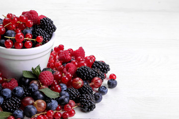 Delicious berries in a bowl, currants, blackberries, blueberries, raspberries on a white wooden table. space for text