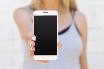 The girl is holding a mobile phone with a blank black screen on an outstretched arm close up. Mockup smartphone for the presentation of the design