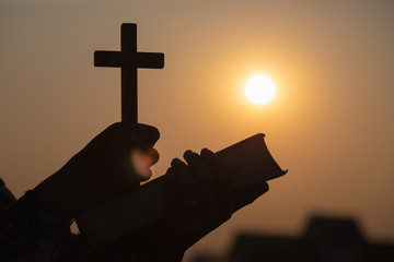 Silhouette of Young woman hands holding holy Bible and lift of christian cross, religion symbol in...