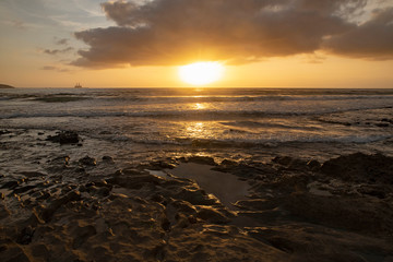 Vibrant, golden sunrise over the limestone coasts of El Medano, Tenerife, Canary Islands, Spain. Mellow light sunrise over the Atlantic with calm waters and a silhouetted oil rig in the distance.