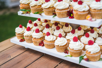 Many cupcakes with white cream and strawberries on a wooden table