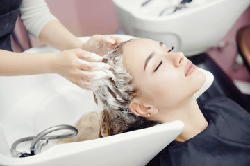 Concept beauty salon. Hairdresser washes hair of beautiful blonde girl under tap in wash