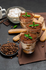 Classic tiramisu dessert in a glass and savoiardi cookies on dark concrete background