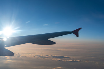 Fototapeta premium Up in the air, view of aircraft wing silhouette with dark blue sky horizon and cloud background in sunset time, viewed from airplane window