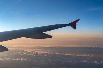 Fototapeta premium Up in the air, view of aircraft wing silhouette with dark blue sky horizon and cloud background in sunset time, viewed from airplane window