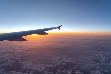 Fototapeta na wymiar Up in the air, view of aircraft wing silhouette with dark blue sky horizon and cloud background in sunset time, viewed from airplane window