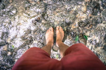 Hiking outdoors in the forest: Cut out of male barefoot feet in a shallow river, fresh water
