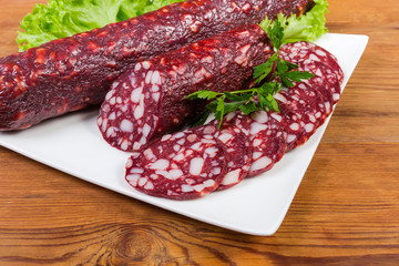 Partly sliced dry-cured sausage on dish close-up