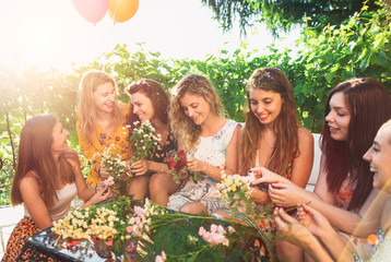 Group of women laughing and having fun making flower bouquet for new bride.